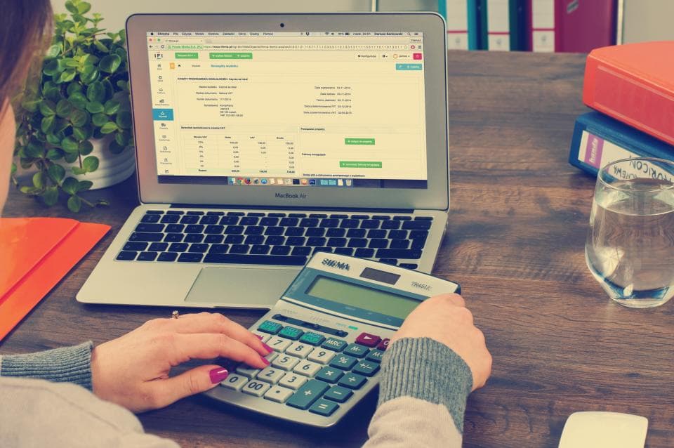Accountant using a calculator next to a laptop showing accounting software