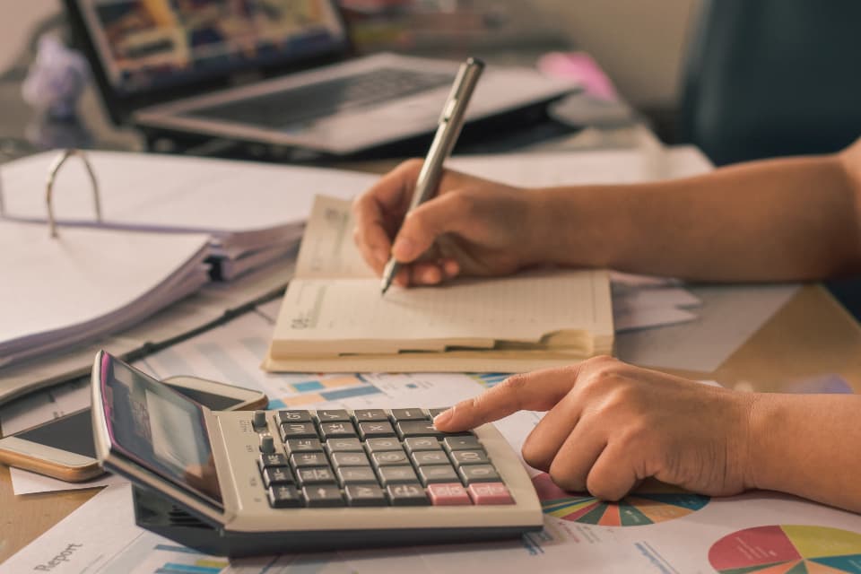 Bookkeeper writing in a ledger while using a desktop calculator