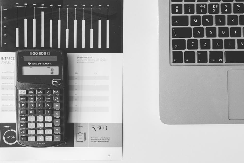 Calculator on top of printed financial charts next to a laptop