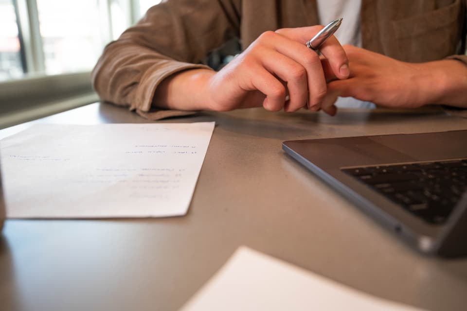 Person reviewing printed documents beside a laptop